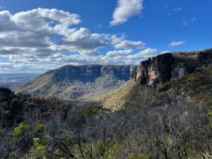 Blue Mountains cliffs with valleys from a lookout overlooking green valleys with a blue sky dotted with white couds