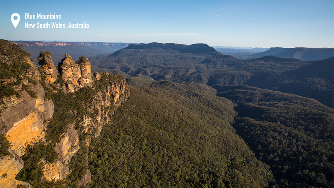  afternoon warm light lighting up one of the top experiences in the Blue Mountains. sandstone cliffs with a spectacular view of a green valley with mountains in the distance